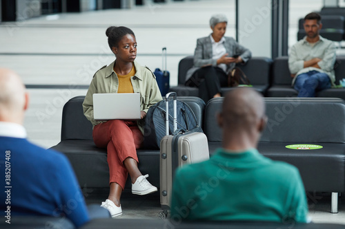 African young woman sitting and using her laptop while sitting at the waiting room of airport