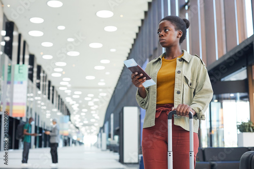 African woman with luggage and tickets standing at the airport and waiting for her flight