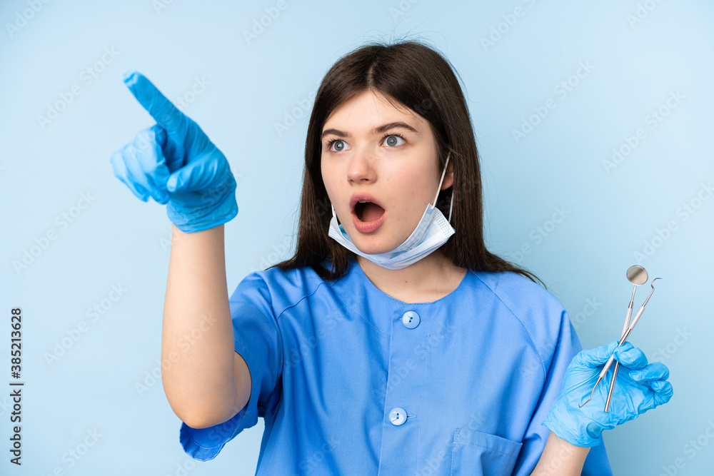 Young dentist woman holding tools over isolated blue background pointing away Young dentist woman holding tools over isolated blue background pointing away