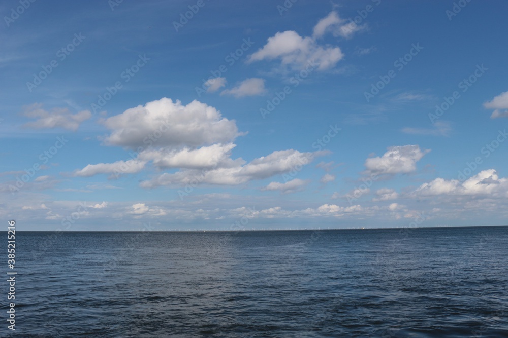 Sea and sky: The rivermouth of the Elbe at high tide in Cuxhaven. Here the Elbe river flows into the North Sea. Far in the distance a wind park is to be perceived. North Germany, Europe.