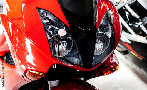 Pair headlights front side view of motorcycle in showroom close up. Glossy red-black windproof shield with headlights of sportbike. Front part of modern motorcycle in salon, with steering wheel Banner © Maksim