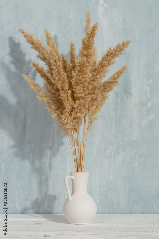 Plakat A vase with yellow spikelets on the table, on a blue background. Light stylish design.
