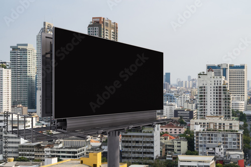 Blank black road billboard with Bangkok cityscape background at day time. Street advertising poster  mock up  3D rendering. Side view. The concept of marketing communication to promote or sell idea.