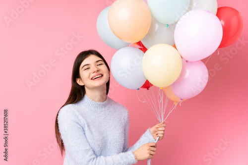 Young Ukrainian teenager girl holding lots of balloons over isolated pink background
