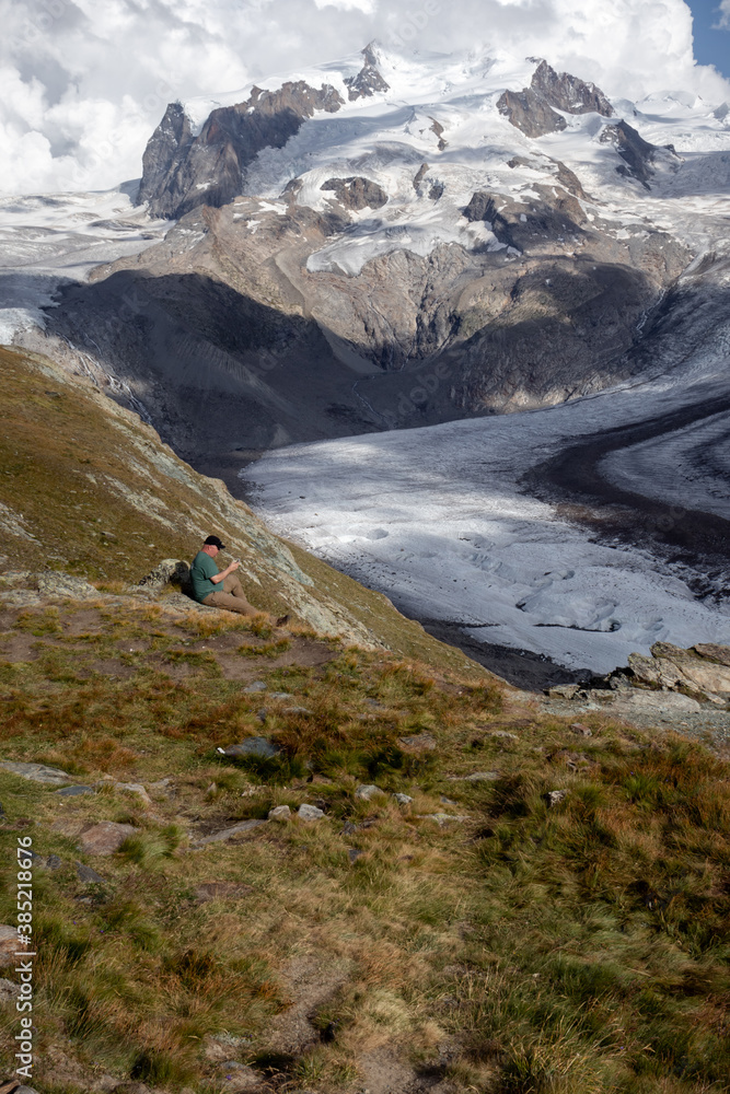 Obraz premium Man sitting on a hill looking at the valley glacier, Gorner, on a summer day in Switzerland. 