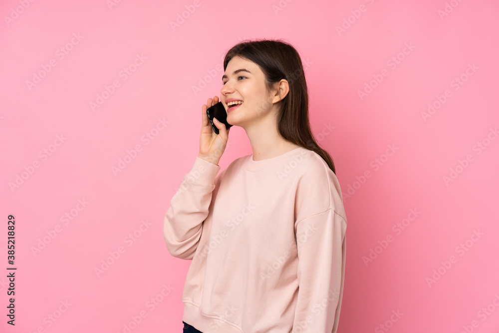 Young Ukrainian teenager girl over isolated pink background keeping a conversation with the mobile phone