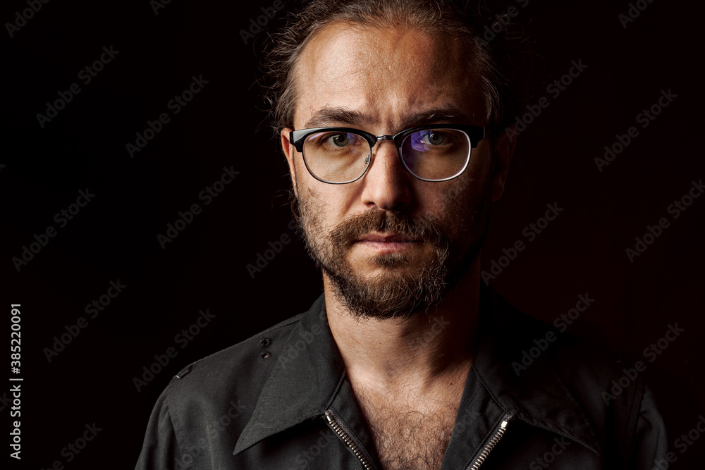 Dark studio portrait of a middle-aged man with beard in glasses Dark studio portrait of a middle-aged man with beard in glasses
