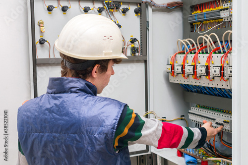 Service of power distribution switchboards. An electrician in an engineering helmet opens the switch box. The technician works in the electrical control room. photo