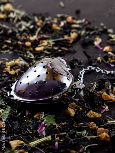 Foldable, metal heart tea infuser, on black. dark background. A sprinkled mix of dry fruits and herbs on the table. Tea drinking concept, wallpaper, close-up. photo