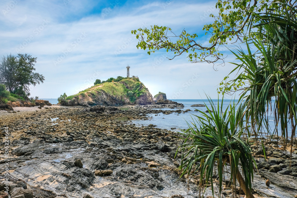 Nice view of the old white lighthouse on the rocky coast. Looking through the vegetation. Landscape from Lanta Island in Thailand