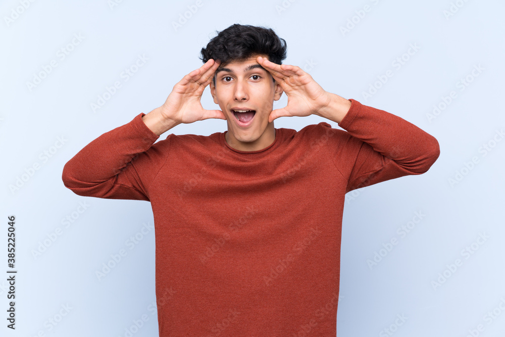 Young Argentinian man over isolated blue background with surprise expression Young Argentinian man over isolated blue background with surprise expression