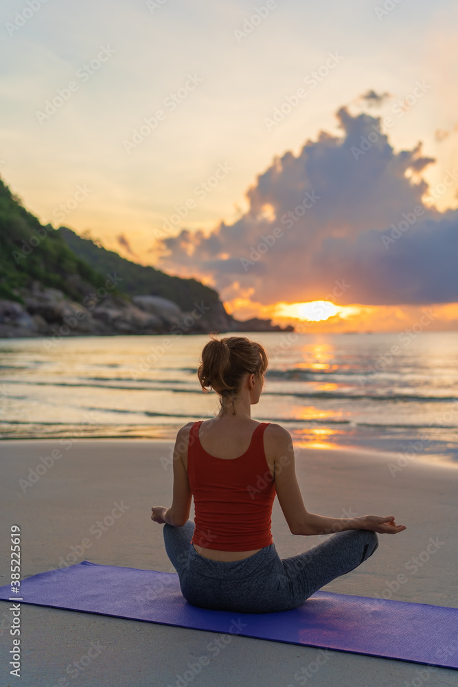 Woman practices yoga. Woman sitting in lotus position and meditating at sunrise on the beach