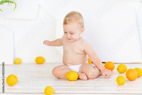a small child a boy six months old plays on the floor in a bright white room in diapers with lemons and oranges