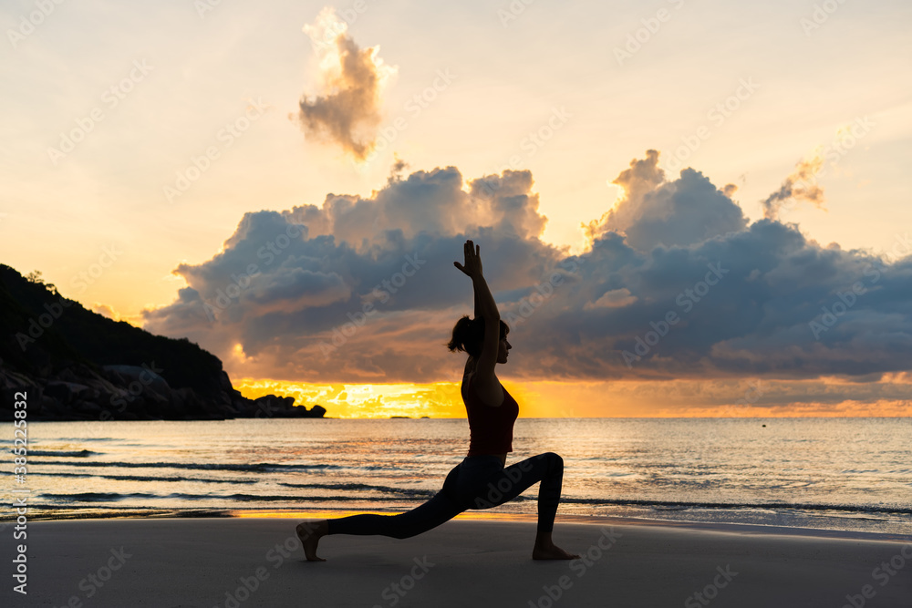 Silhouette of woman practicing yoga on the beach at sunrise