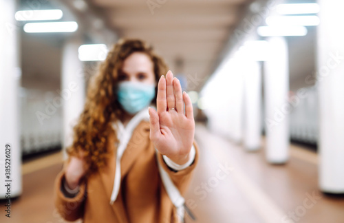 Hand stop sign. Young woman in protective sterile medical mask shows stop hands gesture for stop coronavirus outbreak at subway station. Coronavirus, COVID-19.