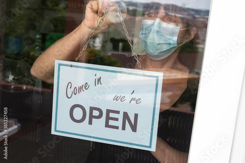 Woman wearing medical face mask hanging open sign on window
