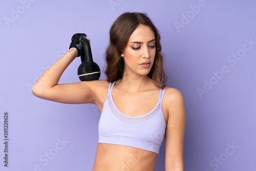Young sport woman over isolated purple background making weightlifting with kettlebell © luismolinero