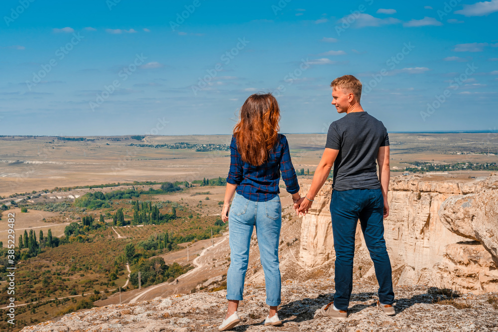 Rear view of a romantic couple a man and a woman standing on the edge of a cliff on a White rock in Crimea with a view of the rural landscape
