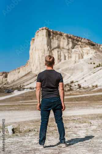 Rear view of a young man standing and looking out over a huge white rock, concept of travel and freedom, Crimea  © KseniaJoyg