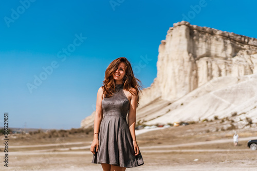 Beautiful young brunette woman in a dress stands on a White rock background in Crimea, summer vacation concept