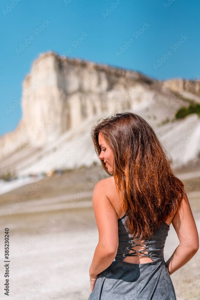 Rear view of a brunette woman in a dress standing against a White rock in Crimea Rear view of a brunette woman in a dress standing against a White rock in Crimea