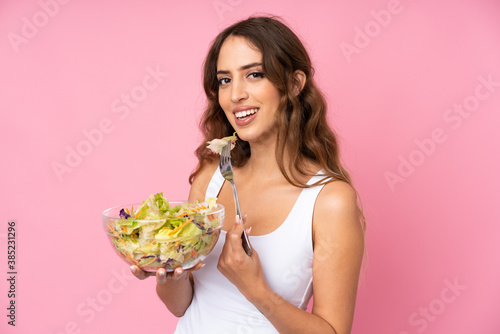 Young woman with salad over isolated pink wall
