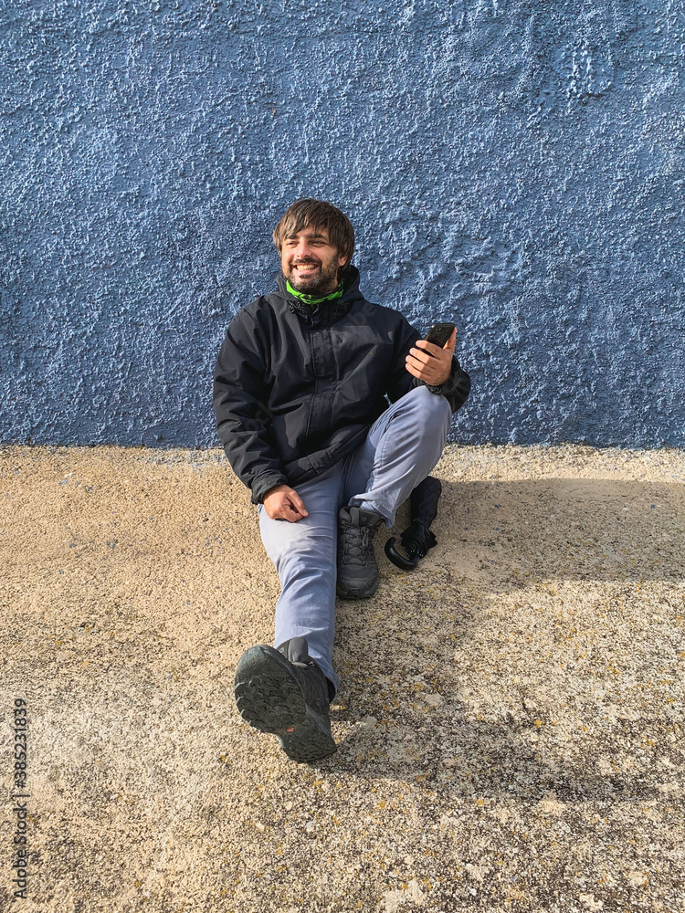 Young man smiling looking at the side while sitting and holding his phone Young man smiling looking at the side while sitting and holding his phone