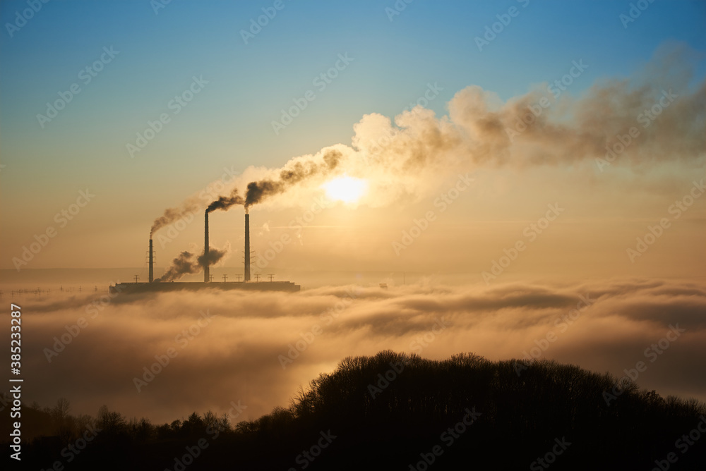 Horizontal snapshot of industrial area at setting sun, three smoking pipes from thermal power station pollute the atmosphere with black smog, concept of man-made disaster and energy generation
