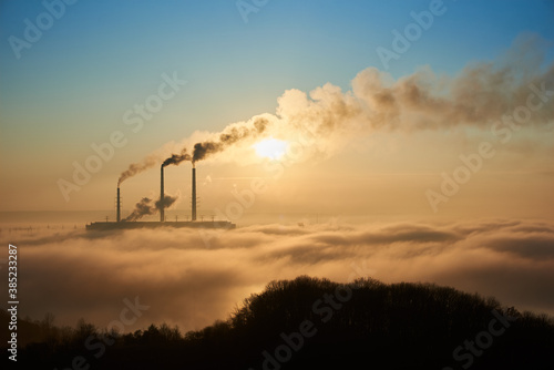 Horizontal snapshot of industrial area at setting sun, three smoking pipes from thermal power station pollute the atmosphere with black smog, concept of man-made disaster and energy generation