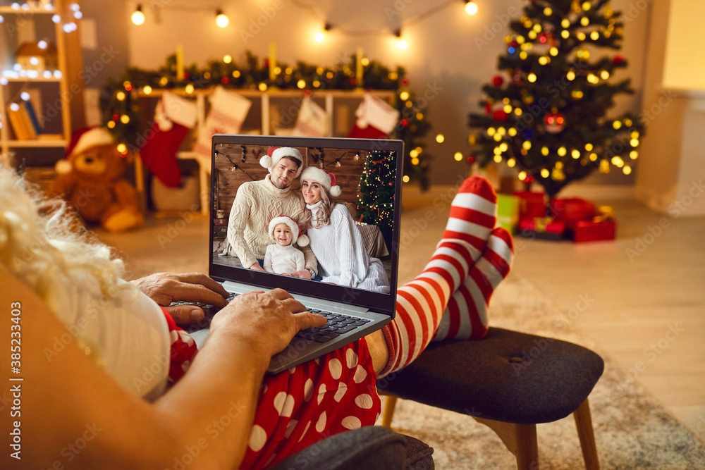 Relaxed Santa with laptop having online video call with happy family on Christmas Day - obrazy, fototapety, plakaty 