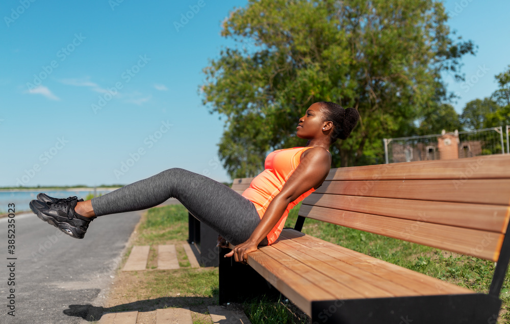 fitness, sport and healthy lifestyle concept - young african american woman exercising with bench at seaside