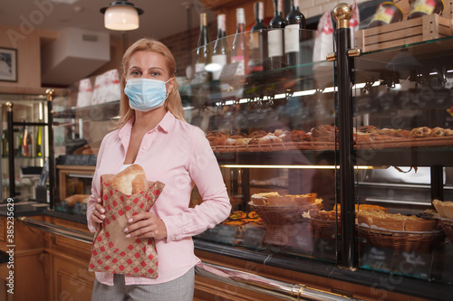 Mature woman buying bread during coronavirus pandemic, wearing face mask