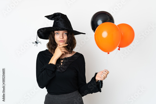 Young witch holding black and orange air balloons thinking