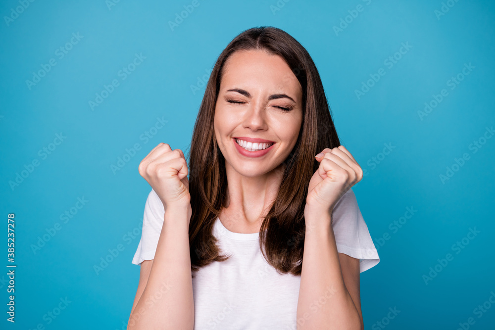 Oh yeah. Closeup photo of attractive funny lady eyes closed good mood charming cute appearance raise fists astonished achievement wear casual white t-shirt isolated blue color background Oh yeah. Closeup photo of attractive funny lady eyes closed good mood charming cute appearance raise fists astonished achievement wear casual white t-shirt isolated blue color background