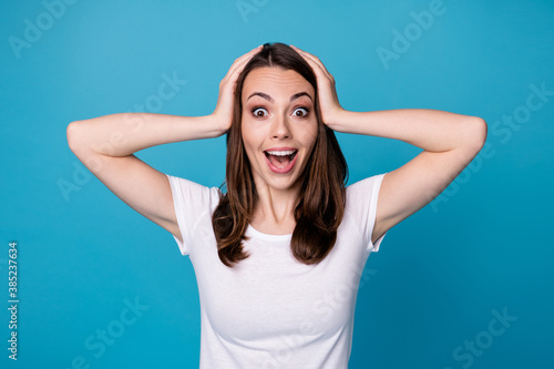 Photo of attractive pretty funny lady good mood charming cute straight hairstyle arms on head shocked amazing news wear casual white t-shirt isolated blue color background