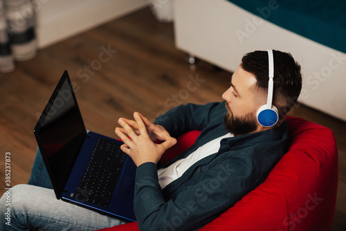 Serious confident man wear headphones and looking at laptop screen. He talking with client distantly. Empty screen for text. 