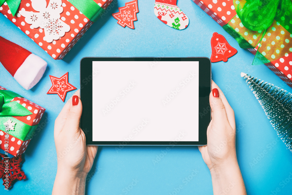 Top view of woman holding tablet in her hands on blue background made of Christmas decorations. New Year holiday concept. Mockup Top view of woman holding tablet in her hands on blue background made of Christmas decorations. New Year holiday concept. Mockup