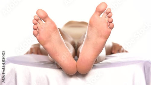 a woman lying on the bed and slowly moving her bare feet on a white background
