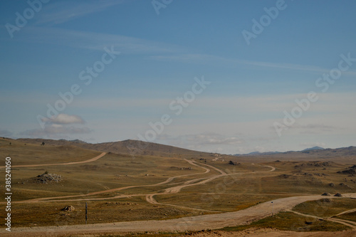 Winding roads in steppe among hills and mountains covered with green yellow grass. Baikal nature. Mountain ranges.