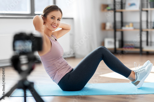 fitness, sport and video blogging concept - happy smiling woman or blogger with camera streaming online tutorial at home
