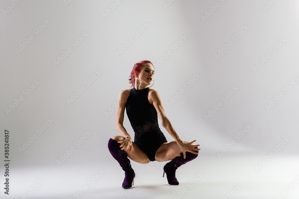 Young beautiful flexible female in black jumpsuit and high heels is posing in a dance studio. Young beautiful flexible female in black jumpsuit and high heels is posing in a dance studio.