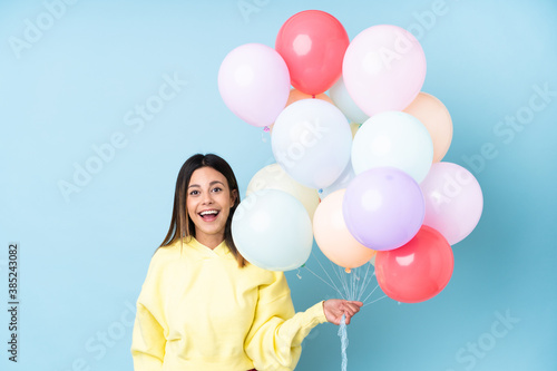 Woman holding balloons in a party over isolated blue background with surprise facial expression