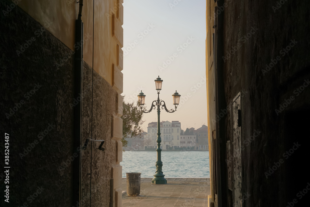 Venezia, Italy - 22/01/18
Dark alley and street light, trash can near the port in the cozy sunshine.
peaceful atmosphere photo.