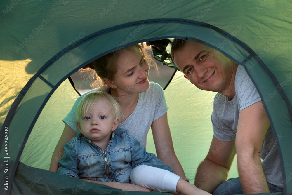Naklejka premium Happy young family with child in tourist tent at the campsite. Vacation with children