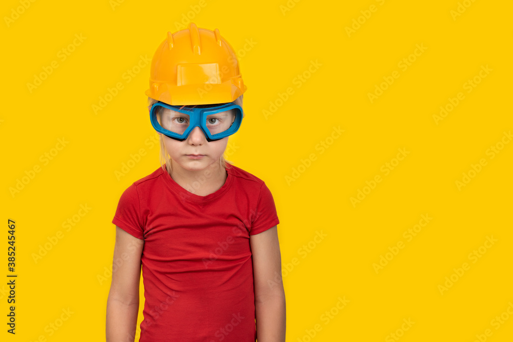 Blond boy in orange protective helmet and safety glasses on yellow background. Copy space Blond boy in orange protective helmet and safety glasses on yellow background. Copy space