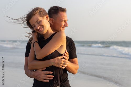 Happy couple of young men and women running, laughing and holding hands on a deserted tropical beach at sunset