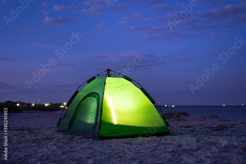 Green tent glows from the inside at night. Camping on the beach.