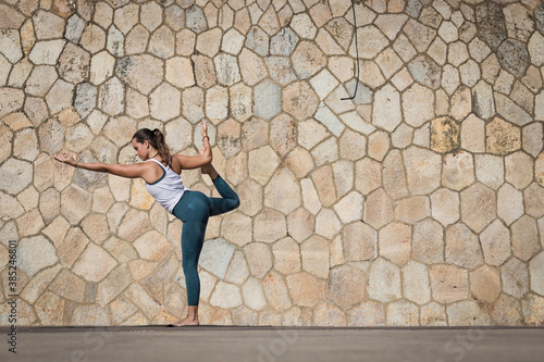 Strong Yoga teacher woman doing an intensive workout along the beach against a seamless pattern wall. Young and attractive woman doing Yoga and Pilates exercises outdoor during a fresh summer day