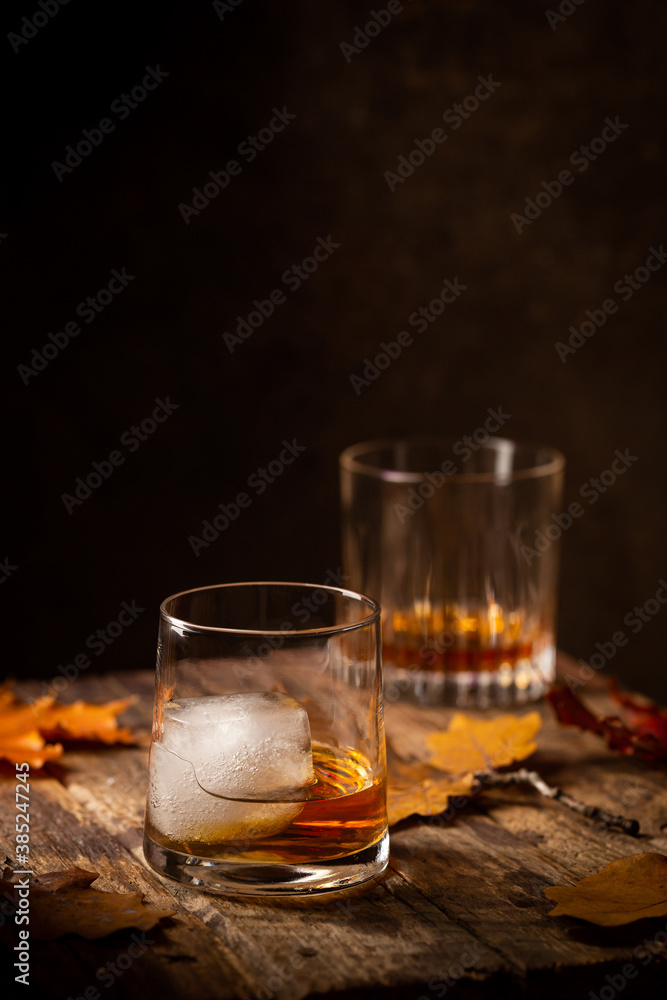 Glass of scotch whiskey and ice on wooden background with autumn leaves Glass of scotch whiskey and ice on wooden background with autumn leaves