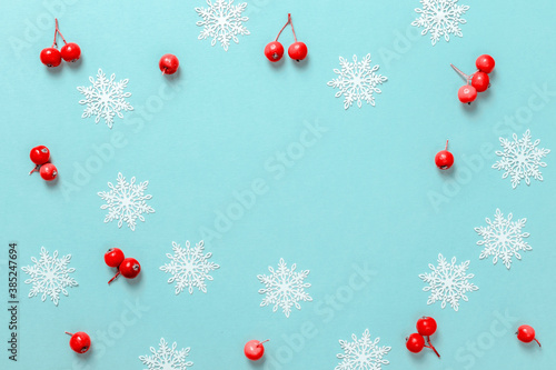 Winter pattern. Red berry, white snowflakes in shape frame on pastel blue background for greeting card. Christmas, winter, new year concept.